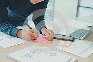 Man writing reminder on sticky note. male freelancer student working organizing plan at workplace