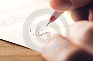 Man writing signature with pen on paper.