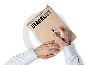 Man writing word Blacklist in notebook on white background, top view