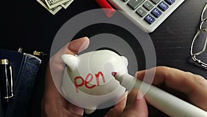 Man writing word pension on a side of piggy bank.