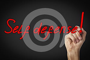 Man writing words Self Defense with marker on glass board against black background, closeup