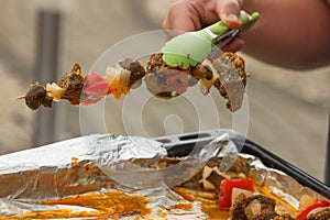 Man's hand holding with green forceps a raw meat skewers in spicy marinade. Ready to cook on grill.