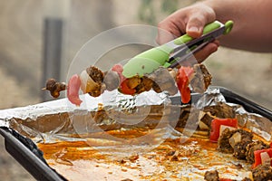 Man's hand holding with green forceps a raw meat skewers in spicy marinade. Ready to cook on grill.