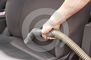 Man& x27;s hand using vacuum cleaner in car. Portable car hoover with tube and hose at work. Cleaning of interior, seats.