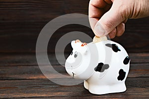 A man's hand puts a coin in the piggy bank on a wooden background.Saving money. Family budget. Money box on a wooden photo