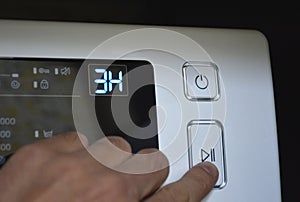 man& x27;s hand on the start button of the washing machine