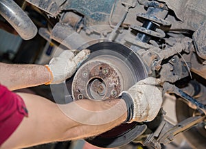 The man& x27;s hands remove the worn and rusty rear brake disc.