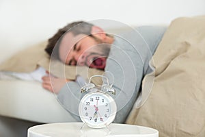 man yawning in bed while alarm ringing