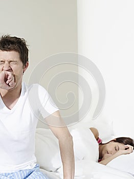 Man Yawning By Woman Sleeping In Bed