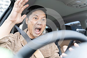 A man is yelling in a car is driving a car and looking at his cell phone. He is surprised and excited