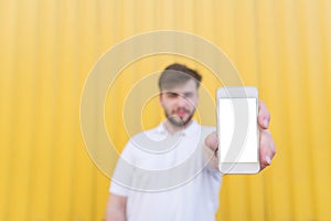Man is on a yellow background and shows the phone with a white screen. Screen for copyspace