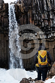 A Man with yellow backpack standing alone at Svartifoss waterfall in Iceland. Travel lifestyle concept