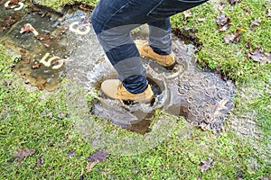 Man in yellow boots plays hopscotch and jumps into squares with numbers flooded with water during a thaw on a playground in the