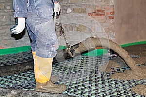 Man in yellow boots pours concrete  over floor heating system