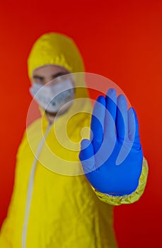 Man in yellow chemical protection suit and face protective mask coronavirus. Gesture stop. Without glasses.