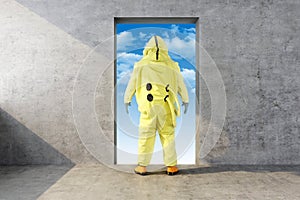 Man in yellow chemical protective suit looks in the opening in the wall with the sky