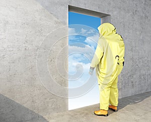 Man in yellow chemical protective suit looks in the opening in the wall with the sky