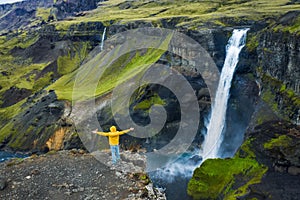 Man in yellow coat raised his hands admiring Haifoss Waterfall in Landmannalaugar canyon, Iceland. Aerial panoramic