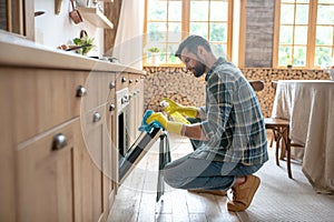 Man in yellow gloves sitting and cleaning the surface in the kitchen