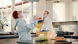 Man in yellow hoodie holds rainbow flag in kitchen with houseplant and tableware