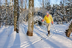 A man in a yellow jacket i walking on snowy woods on wooden skis