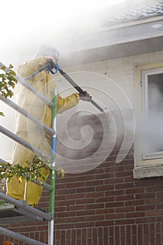 Man in yellow rain suit cleans paint from brick wall of house fa