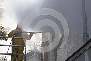 Man in yellow rain suit cleans paint from brick wall of house fa