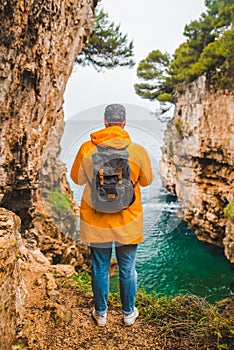 man in yellow raincoat standing on the cliff of canyon looking at sea