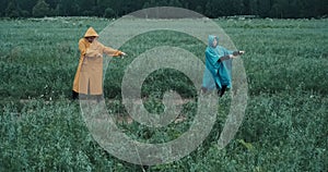 Man in yellow raincoat and a woman in blue raincoat dance in a field