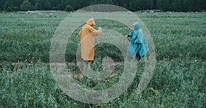 Man in a yellow raincoat and a woman in a blue raincoat dance a twist in a field