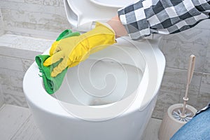 Man in yellow rubber gloves cleaning toilet seat with green cloth. Bathroom and toilet hygiene. Hand cleaning toilet bowl in