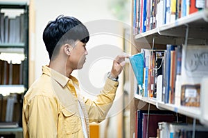 A man in a yellow shirt is looking at a book on a library shelf