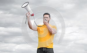 man in yellow shirt shouting in loudspeaker on sky background