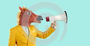 Man in yellow suit and funny horse mask speaking through megaphone on blue background