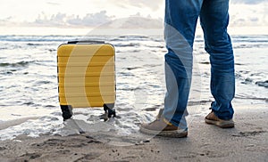 Man with yellow suitcase relaxing alone on the seaside at sunset. Man waiting for a cruise ship Travel Lifestyle concept