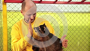 Man in a yellow sweater strokes raccoon, love for animals. Coon captivity, zoo.