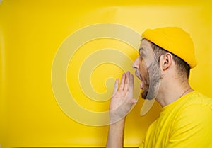 Man in a yellow T-shirt and a casual hat stands on a yellow background and shouts into an invisible gramophone. place for your tex