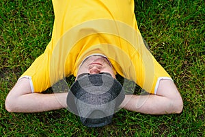 Man in yellow T-shirt and hat lying on the grass