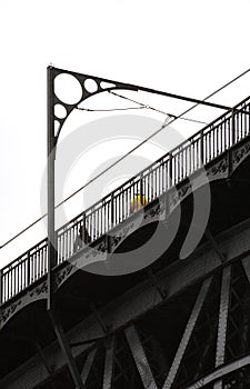 Man in yellow t-shirt and woman dressed in black with long hair, walking on the top of the Don Luis I steel bridge in Porto with