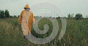 Man in yellow in a yellow raincoat with a hood walks through a field with grass