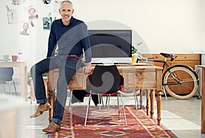 The man you want leading your team. Portrait of a casually-dressed mature man sitting on his desk in an office.