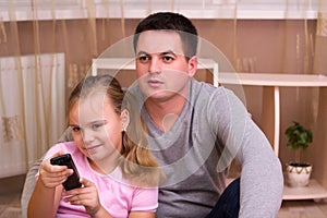 Man and young girl in living room with remote control smiling.