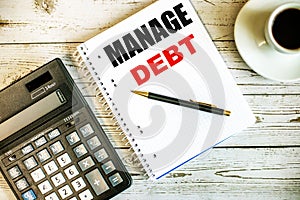 MANAGE DEBT is written on a white notepad near the coffee and calculator. Business concept