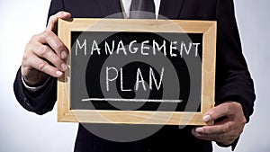 Management plan written on blackboard, business person holding sign, strategy