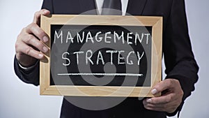 Management strategy written on blackboard, businessman holding sign, concept