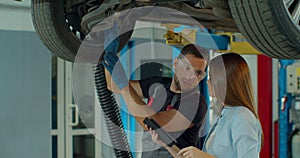 Manager checks data on a tablet computer and explains the breakdown to a mechanic. Car service employees inspect the