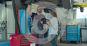 Manager checks data on a tablet computer and explains the breakdown to a mechanic. Car service employees inspect the