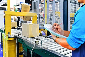 Manager engineer checking cardboard boxes on conveyor belt in distribution warehouse