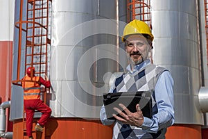 Manager or Engineer With Digital Tablet Standing in front of Oil Refinery Storage Tanks