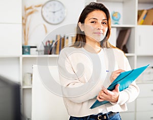 Manager girl is standing in the office and filling out documents on a folder